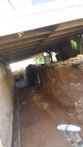 Sous un bâtiment : un étroit tunnel de terre, avec des poutres de soutien et un seau visibles.