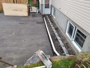 Vue extérieure d'une tranchée en béton avec un tuyau blanc à côté d'un bâtiment avec des fenêtres et une porte.