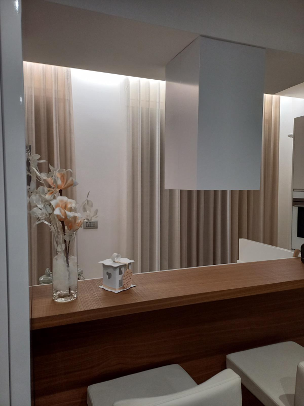 Interni moderni con bancone in legno, lampada a sospensione bianca, vasi e sgabelli accanto a tende a righe.