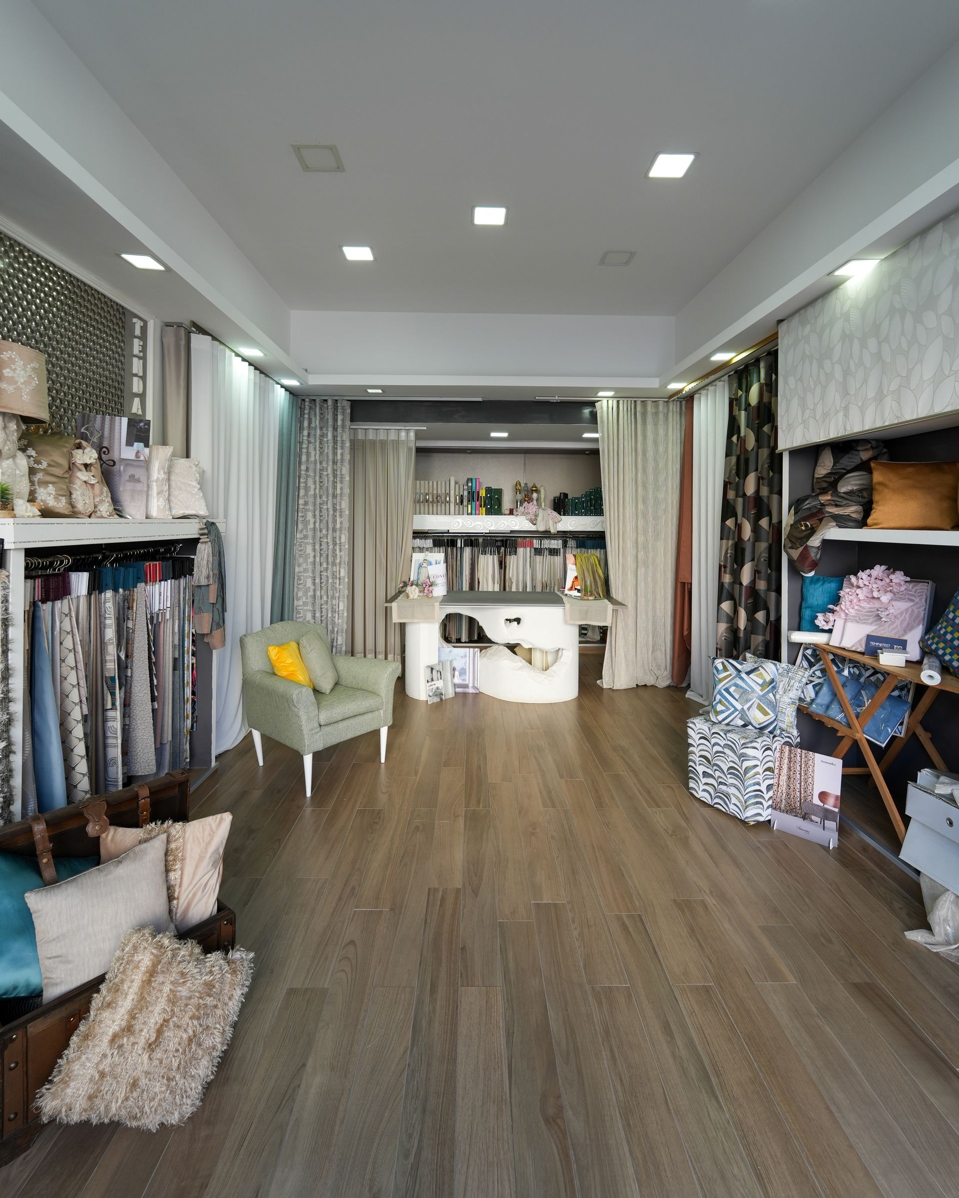 Interno di una boutique di abbigliamento con stender, scaffali e un tavolo espositivo centrale, illuminato da vivaci luci a soffitto