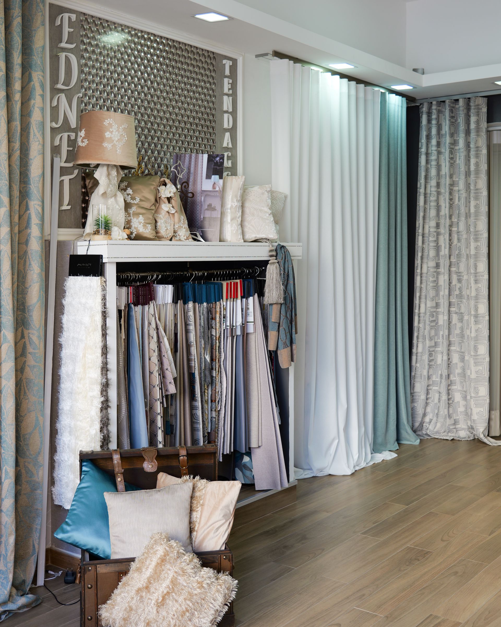 Showroom di tende con campioni di tessuto appesi, scaffali e cuscini decorativi in uno spazio espositivo luminoso