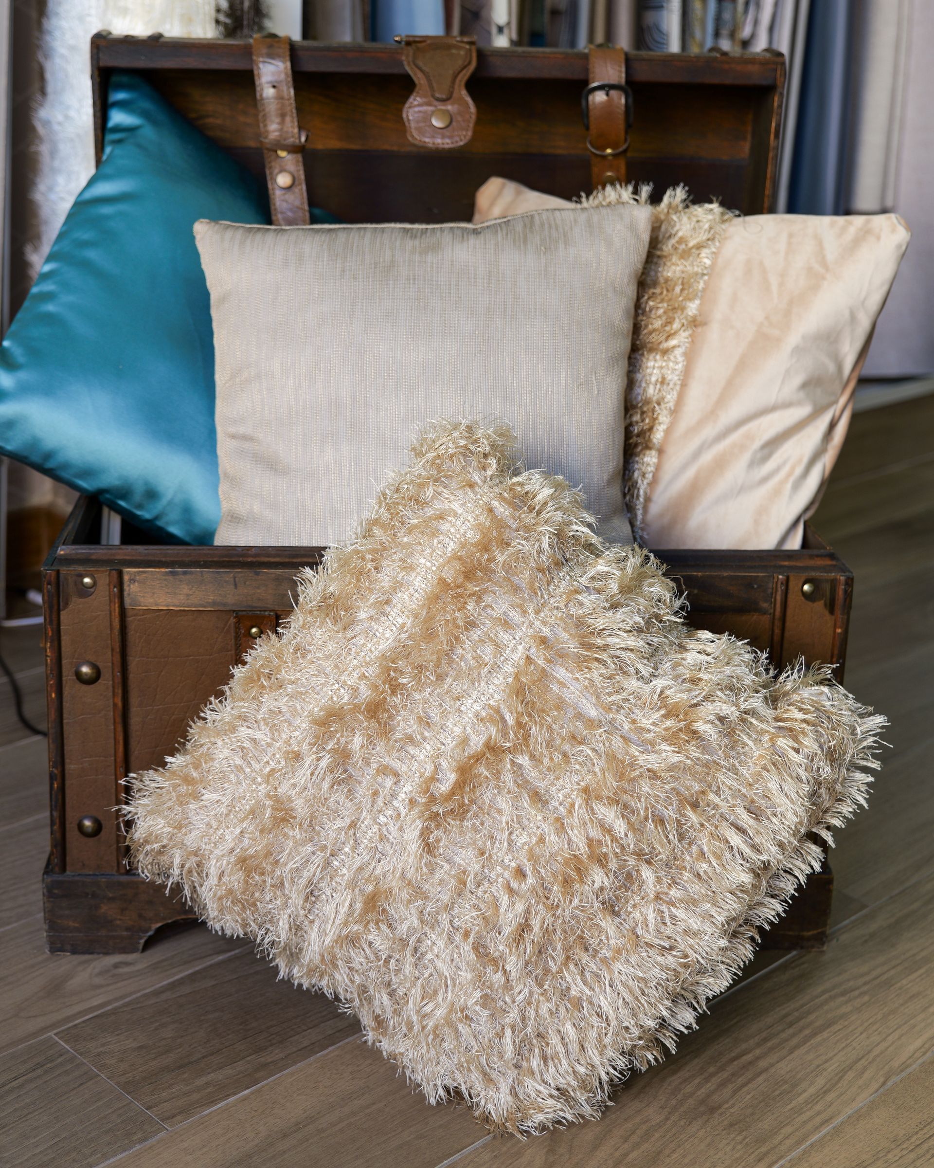 Cuscini decorativi su una valigia vintage, tra cui cuscini materici color verde petrolio, beige e crema