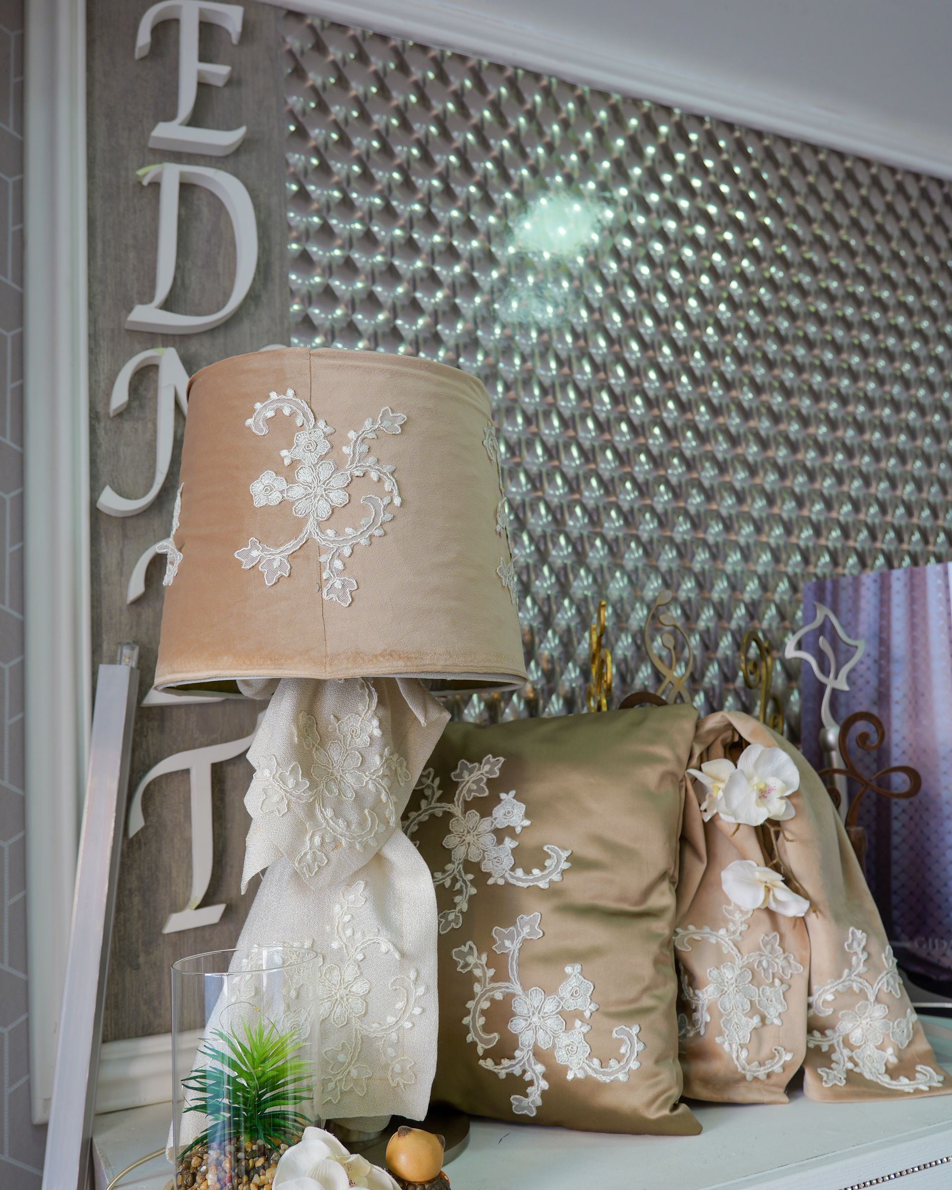 Lampada decorativa e cuscini floreali su un letto accanto a un pannello da parete decorato.