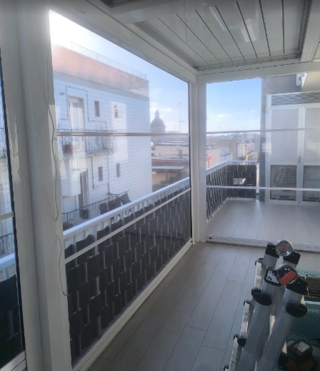 Balcone con pavimento piastrellato, ringhiera, attrezzi per allenarsi e vista sugli edifici vicini sotto un cielo luminoso