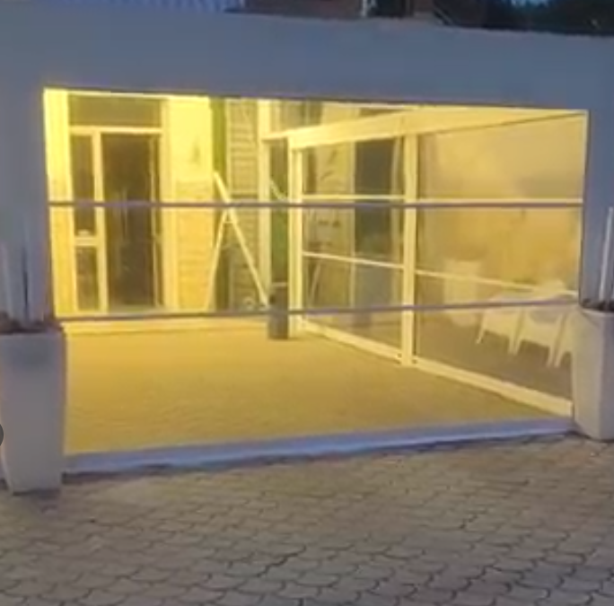 Ingresso di un edificio illuminato da una luce gialla, con un cancello di metallo e un vialetto lastricato al crepuscolo