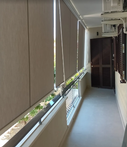 Stretto corridoio balcone con tende beige, fioriere sulla ringhiera e un condizionatore da finestra.