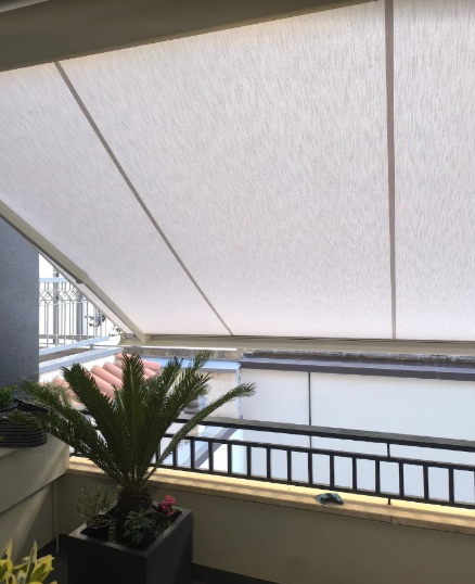 Balcone con tenda da sole bianca, vista sulla città e una palma in vaso in primo piano