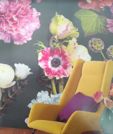Poltrona giallo senape con cuscino viola davanti a un murale floreale sulla parete