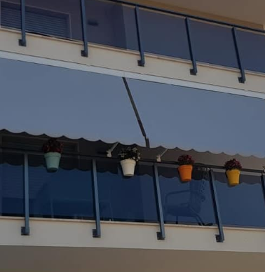 Balconi con finestre blu e vasi di fiori colorati sotto una tenda da sole a righe