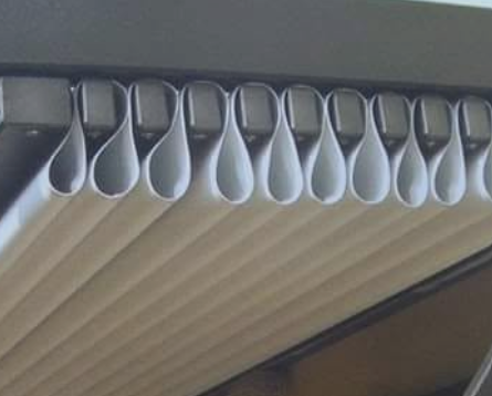 Fila di tubi cilindrici bianchi appesi al soffitto, ripresi da vicino dal basso.
