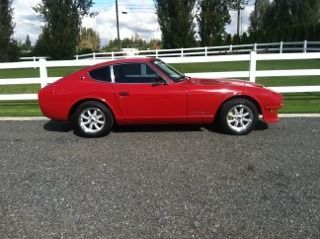 A red sports car is parked in front of a white fence.