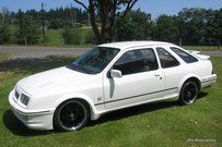 A white car is parked in the grass next to a road.