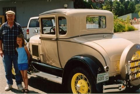 A man and a little girl standing next to an old car with a license plate that says 6028