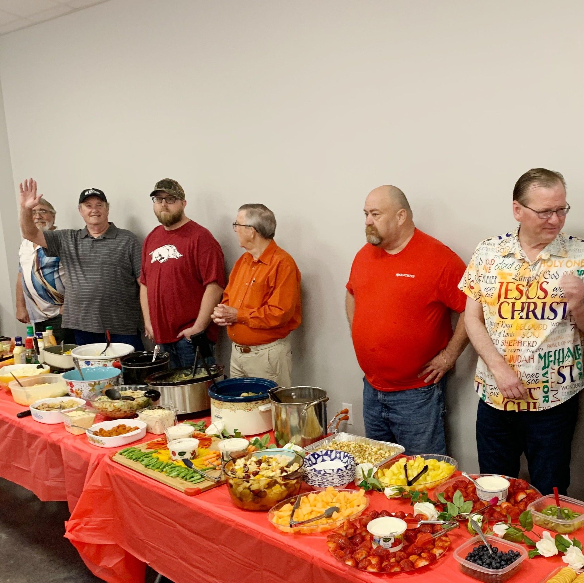 People serving buffet dishes at a long red table in a bright room