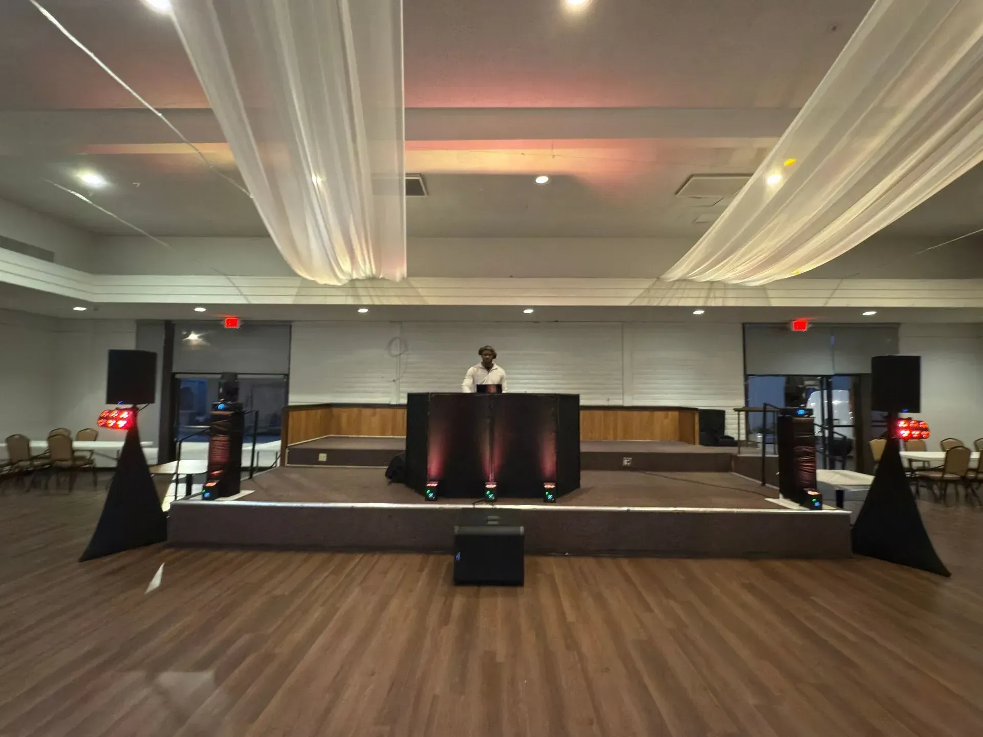 Outdoor stage setup with yellow steps, black drapes, speakers, and floral decorations under a blue sky