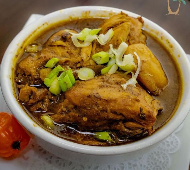 Bowl of Jamaican Brown Stew Chicken, garnished with scallions, and a red pepper on the side.