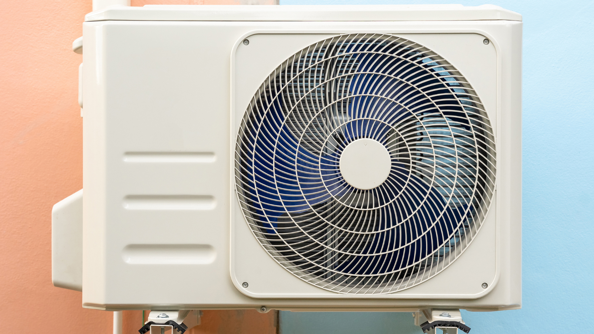 White air conditioner unit mounted on a wall with fan exposed.