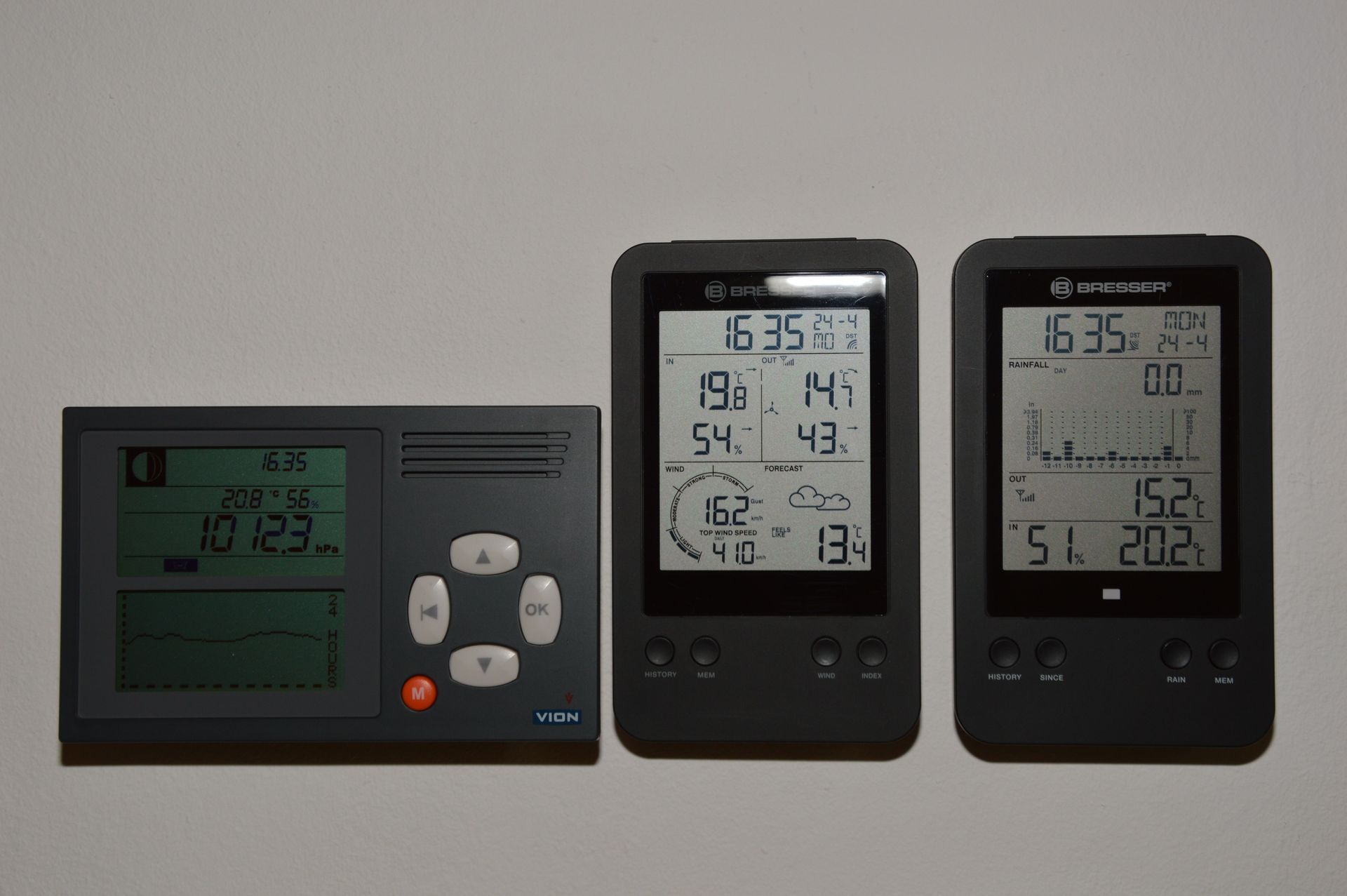 Three digital weather stations on a shelf, two black and one gray with LCD readings.
