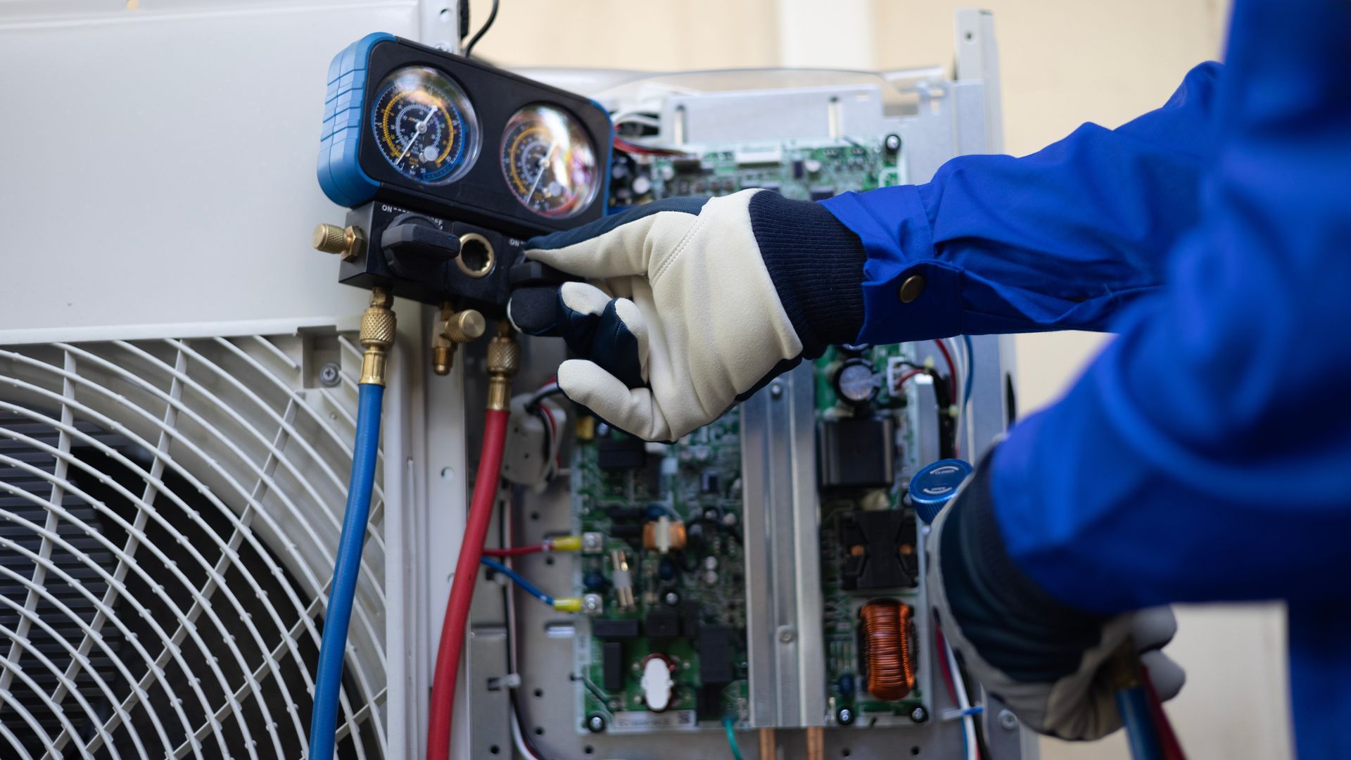 HVAC technician in blue overalls adjusts gauges on an air conditioner unit.