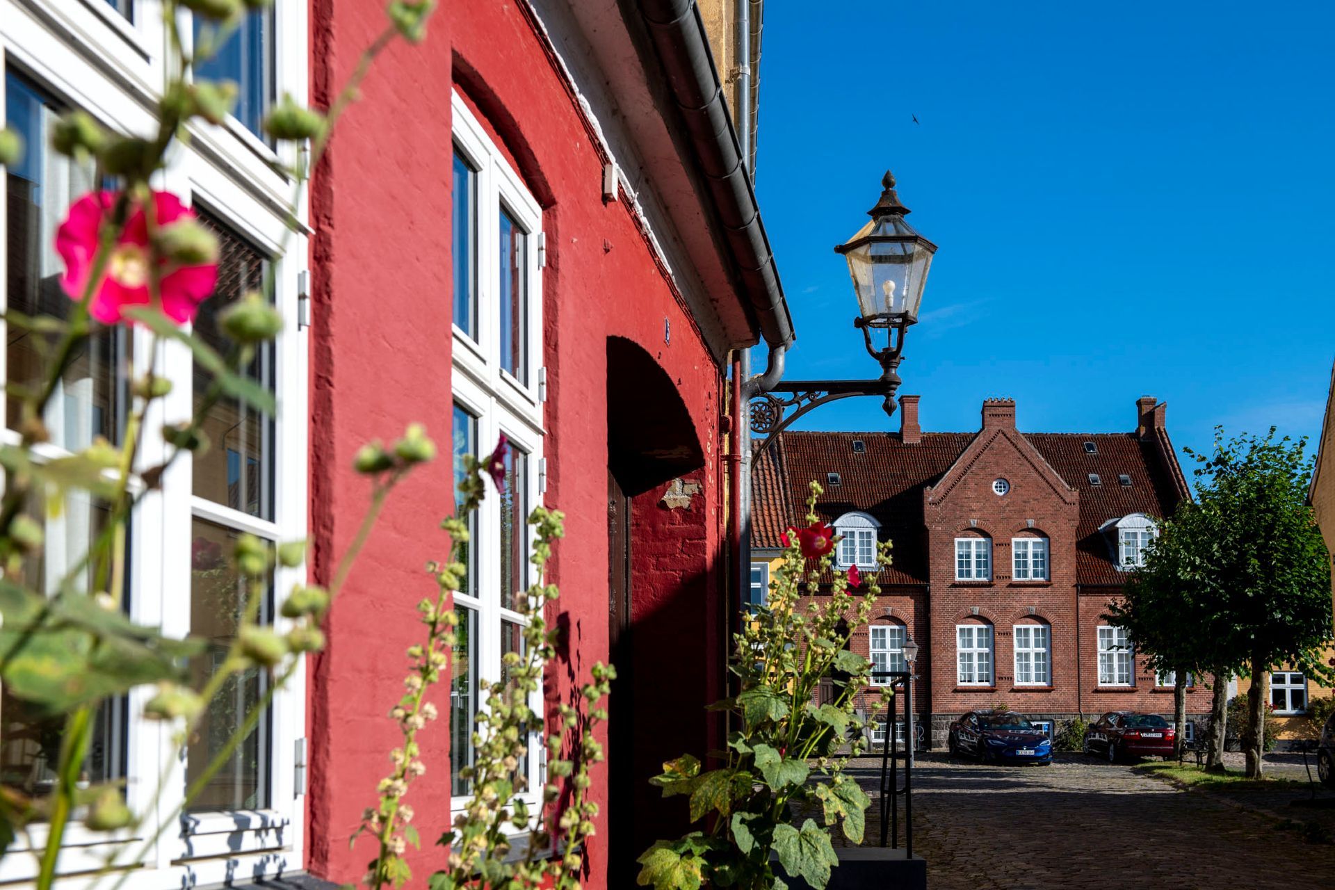 Rød bygning i Præstø med havnen i baggrunden og med en blå himmel.