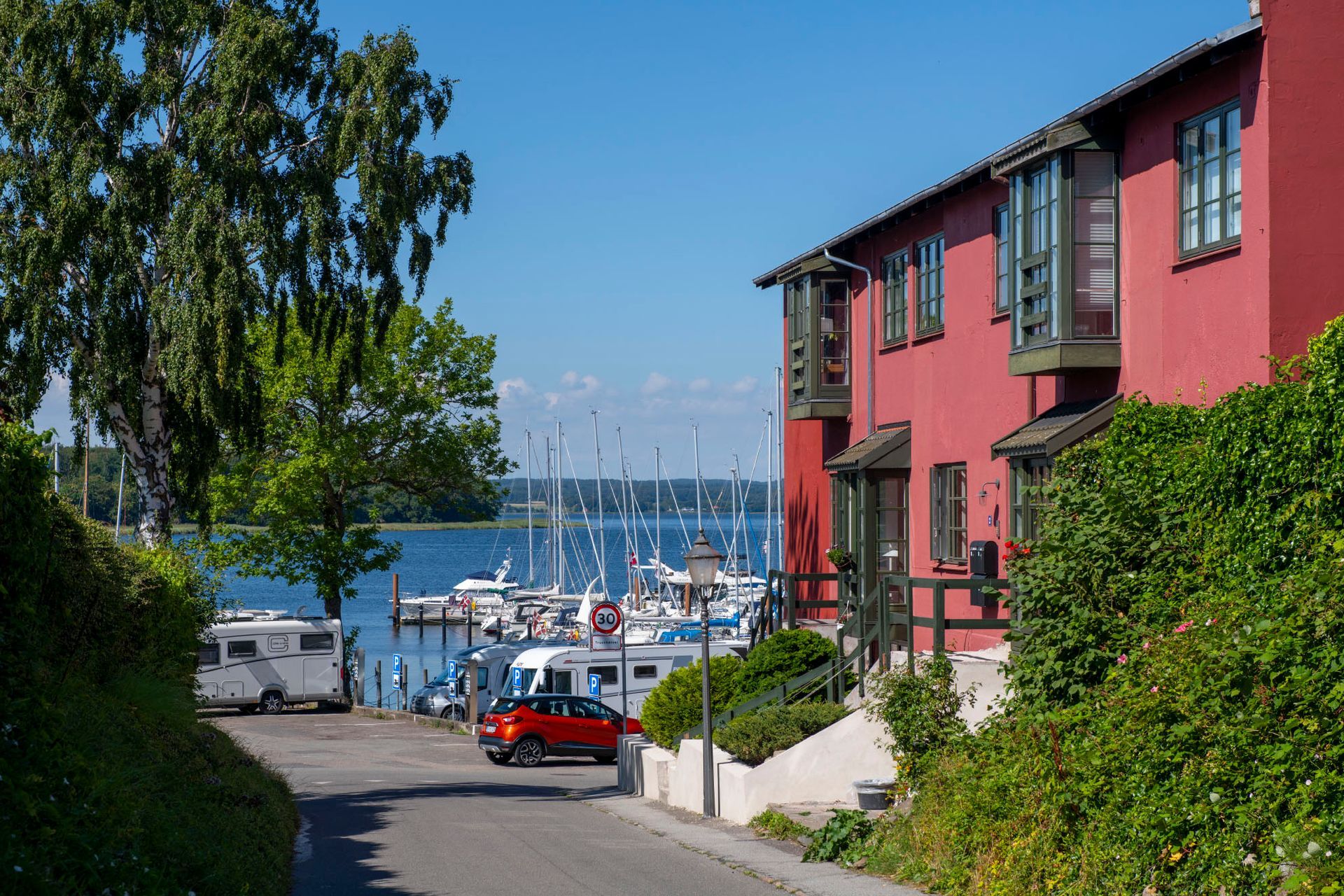 Rød bygning i Præstø med havnen i baggrunden og med en blå himmel.