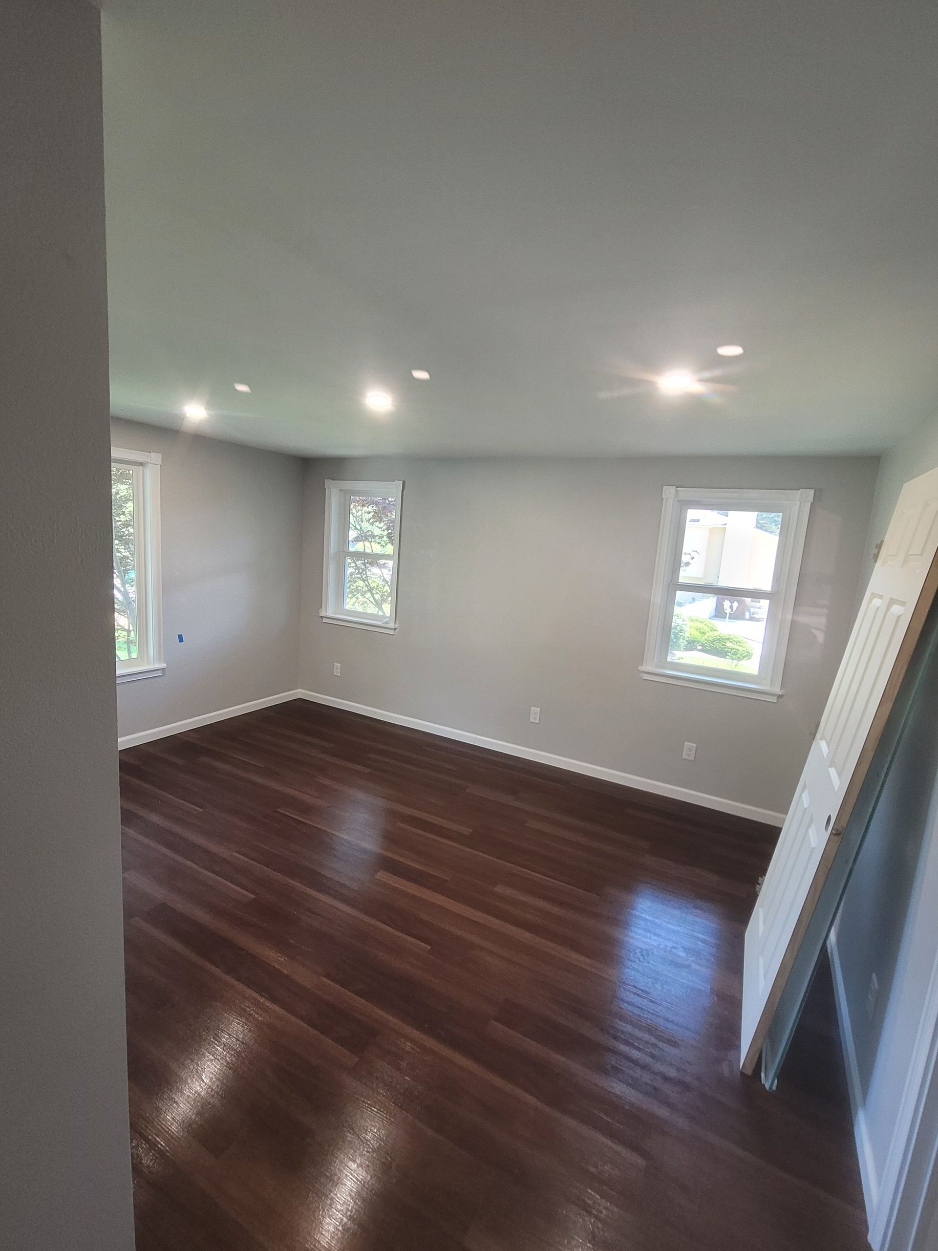 A large empty room with hardwood floors and three windows.