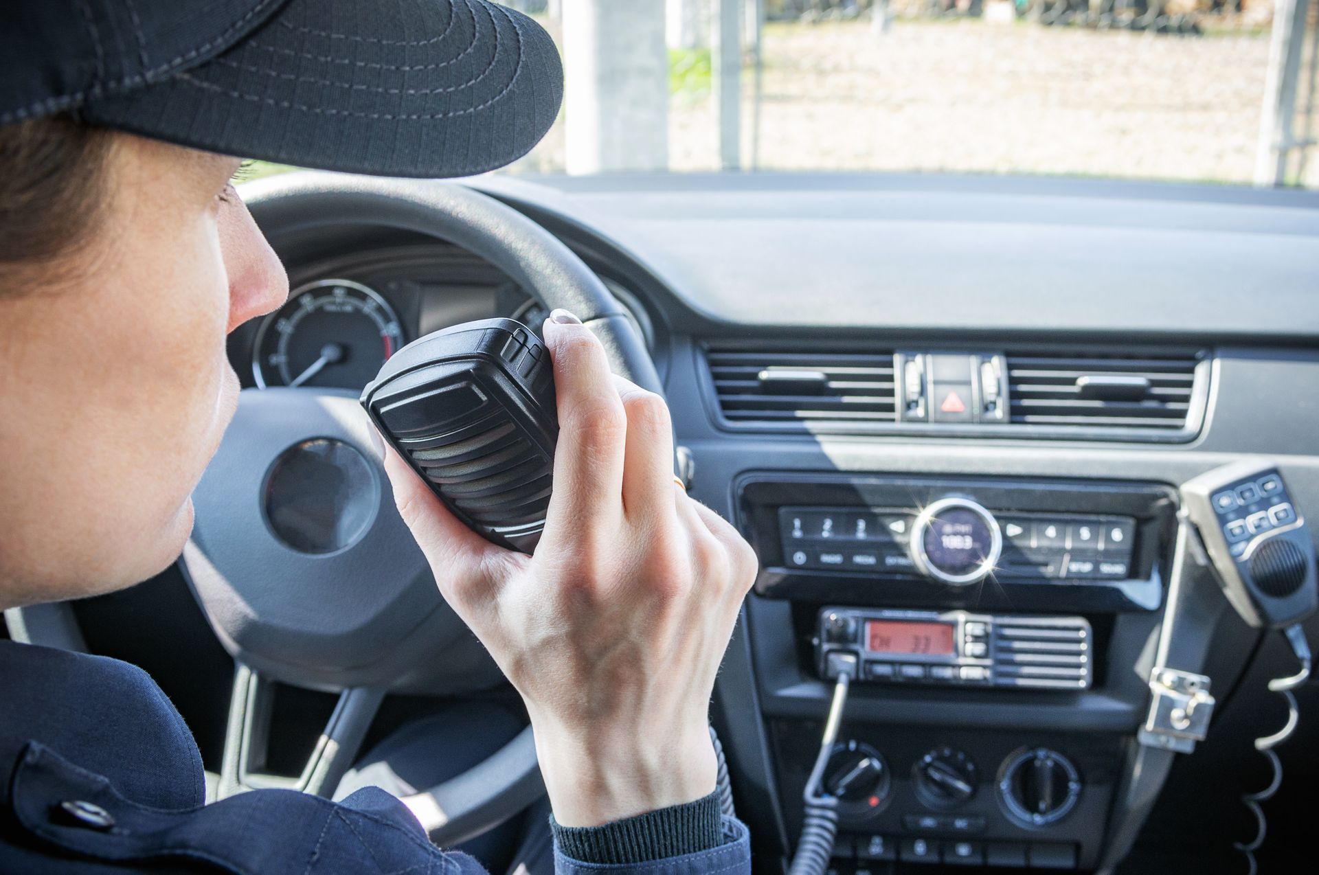 De bestuurder gebruikt een portofoon terwijl hij in de auto zit, met de bedieningsknoppen op het dashboard zichtbaar.