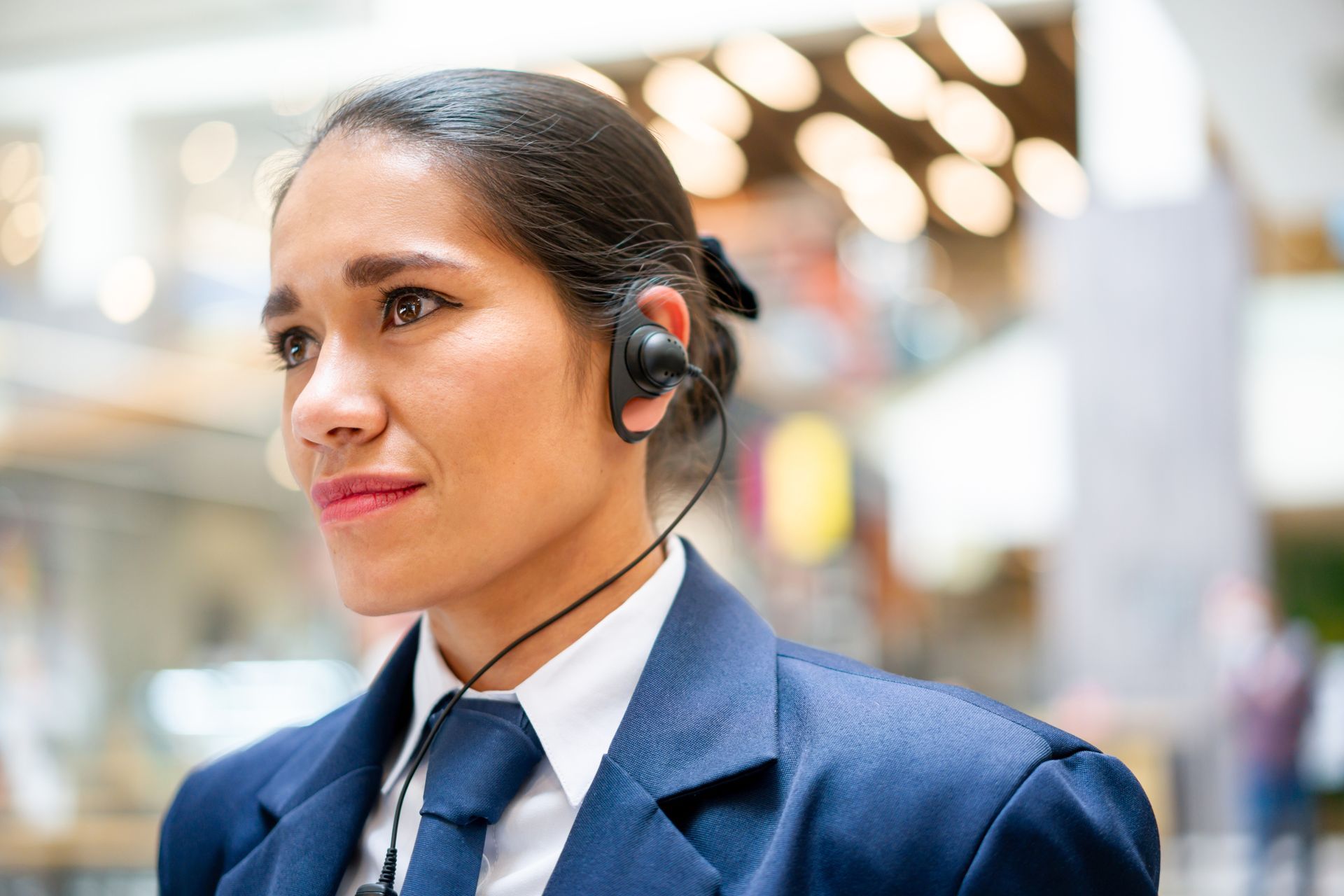 Vrouw in een blauw pak met een headset op, staand in een lichte kantooromgeving.