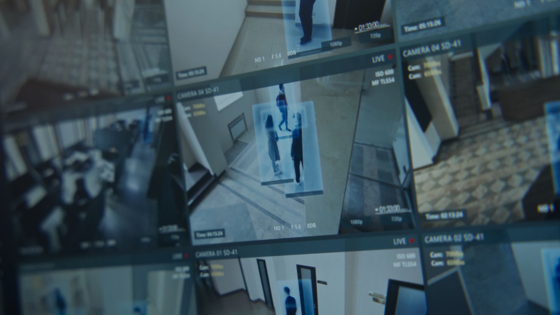 Bewakingsmonitorwand met beelden van meerdere CCTV-camera's die een gang en voorbijlopende mensen tonen.