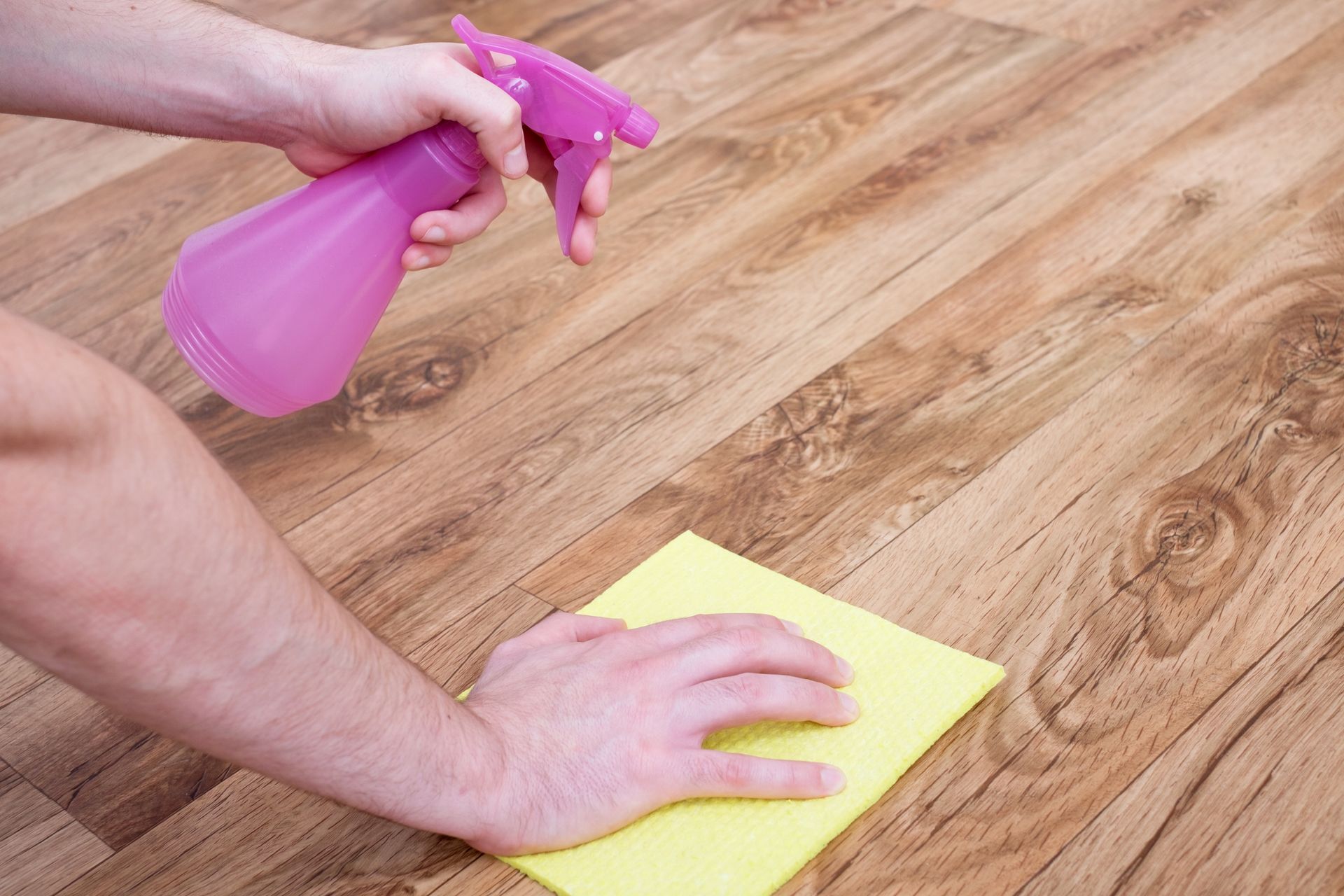 Hand spraying cleaner onto a yellow cloth on a wooden floor
