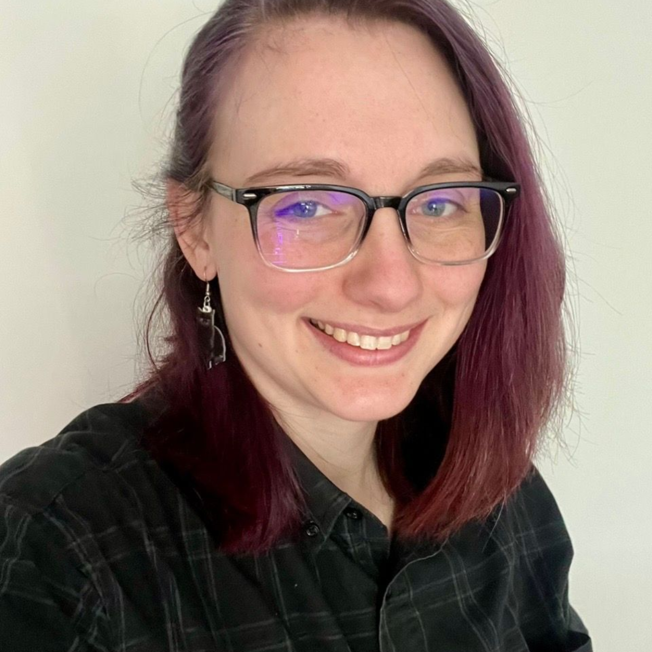 Smiling white woman with black top rimmed glasses, with blue eyes and brown hair with pink infused highlights.