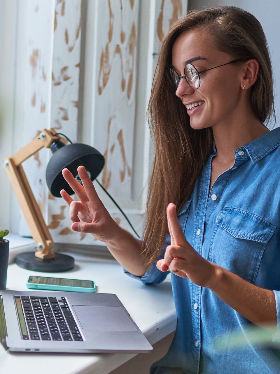 Woman smiling, dark blonde hari with round black rimmed glasses. Looking at the laptop.