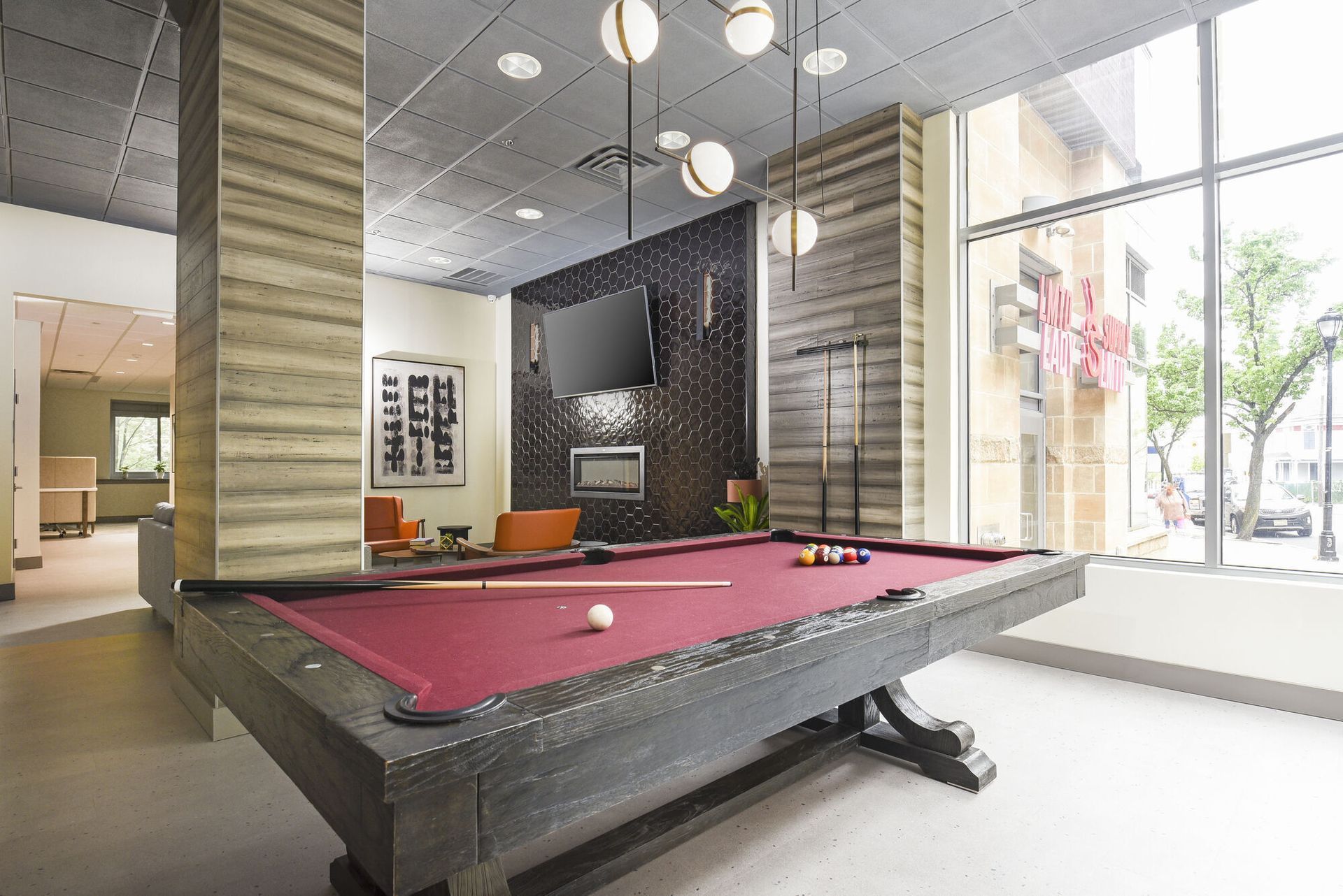 Indoor community lounge with a dark pool table, seating, and large windows.