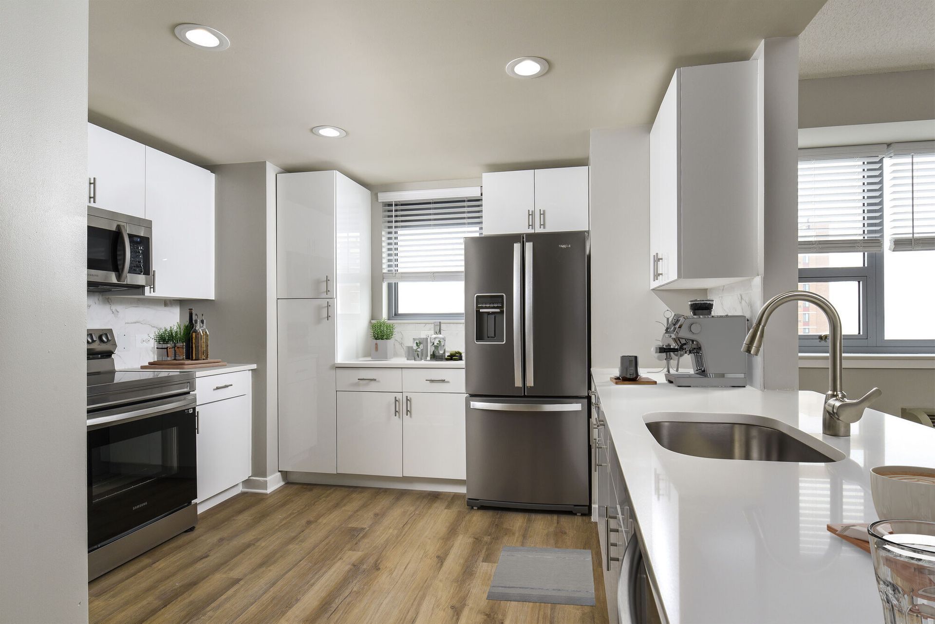 Modern white kitchen with stainless steel refrigerator, oven, microwave, and an island sink.