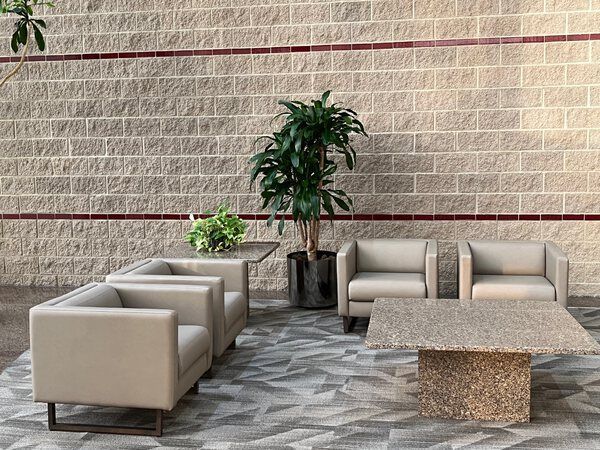 Lounge area with tan couches, terrazzo tables, and a large plant against a textured brick wall.