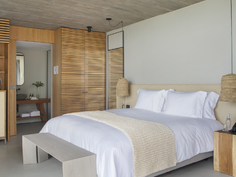 Quarto moderno com cama branca, parede com ripas de madeira e decoração em cinza claro.