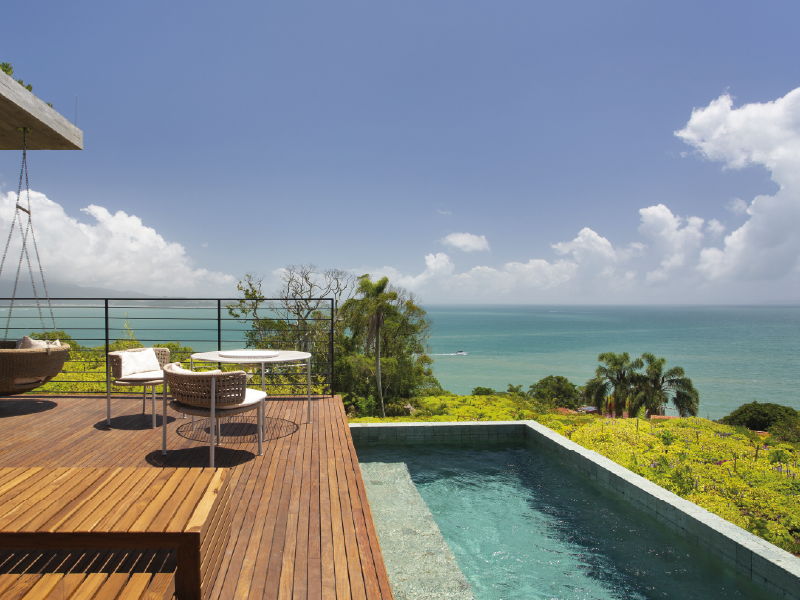 Terraço à beira-mar com pátio de madeira, piscina e mar turquesa sob um céu claro.