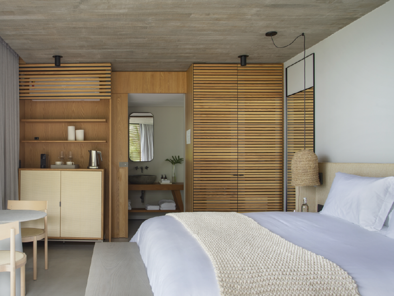 Quarto moderno com prateleiras embutidas de madeira, portas de correr no armário e cama com roupa de cama branca.