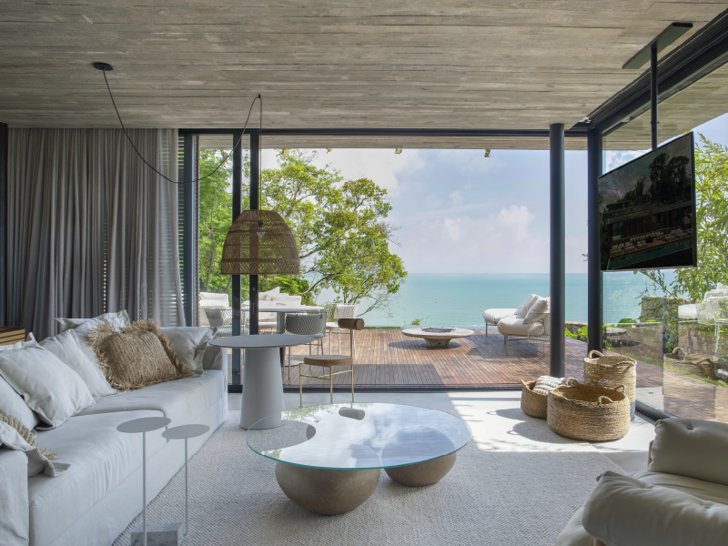 Sala de estar moderna com acesso a um pátio com vista para o mar, piscina e espreguiçadeiras brancas.