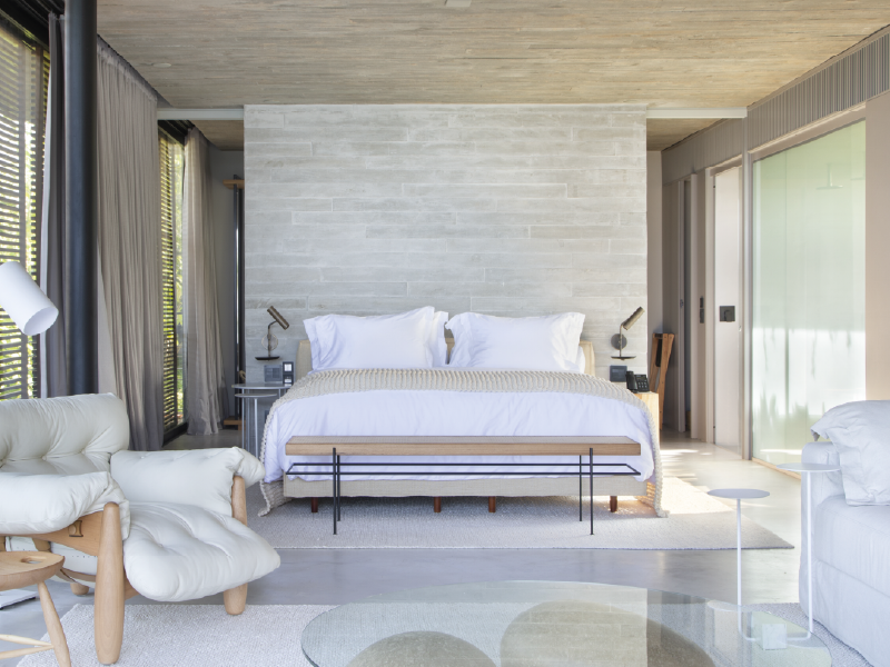 Quarto moderno com cama grande, decoração neutra e janelas do chão ao teto com vista para uma varanda.