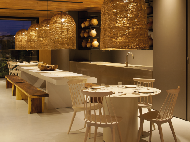 Área de jantar moderna do restaurante com mesas de madeira, cadeiras de vime e iluminação pendente aconchegante.