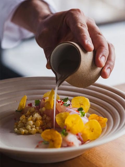 Despejar o molho à mão sobre um prato gourmet decorado com milho, flores e guarnições.