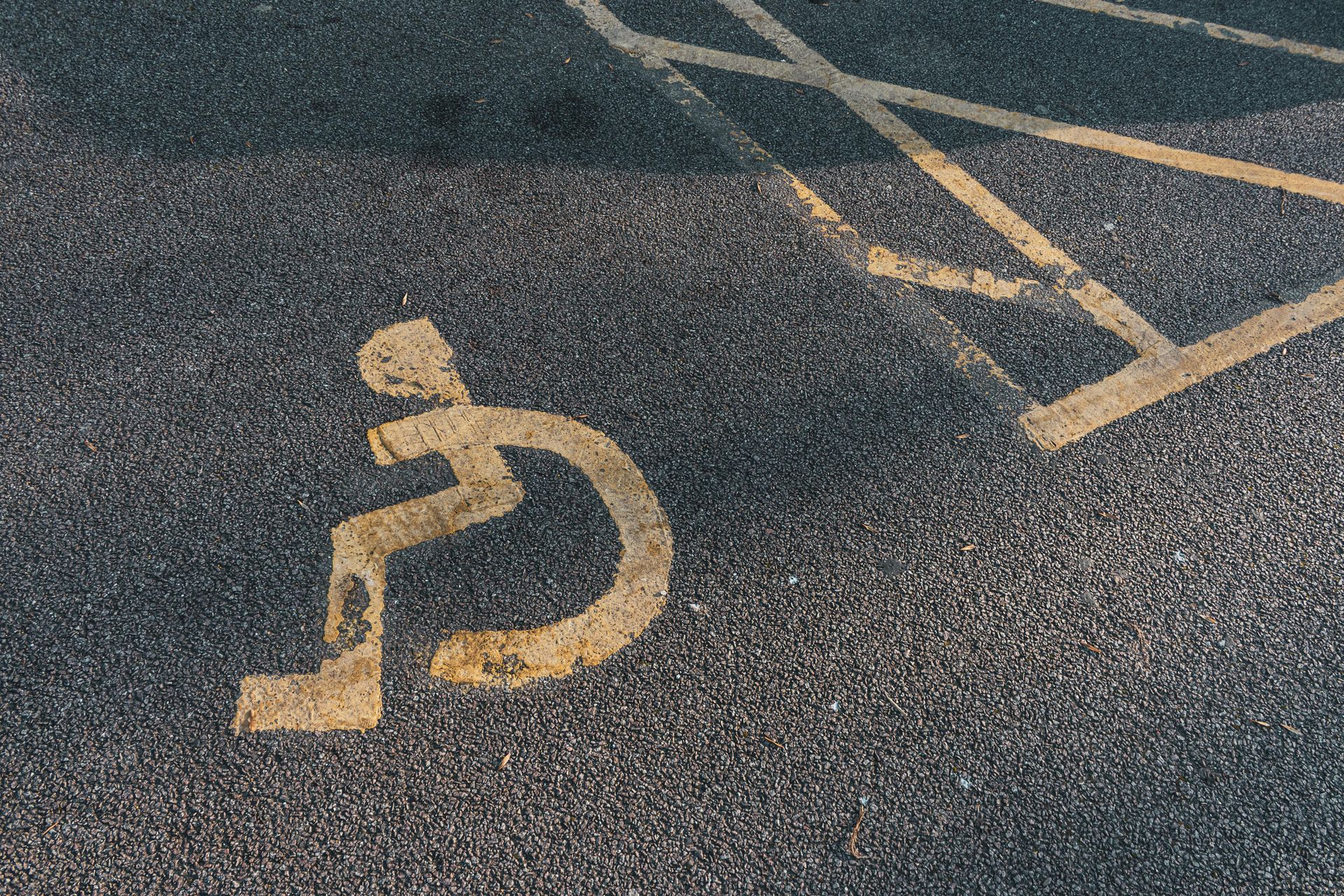 A faded white international symbol of access painted on dark asphalt next to a yellow cross-hatched parking zone.