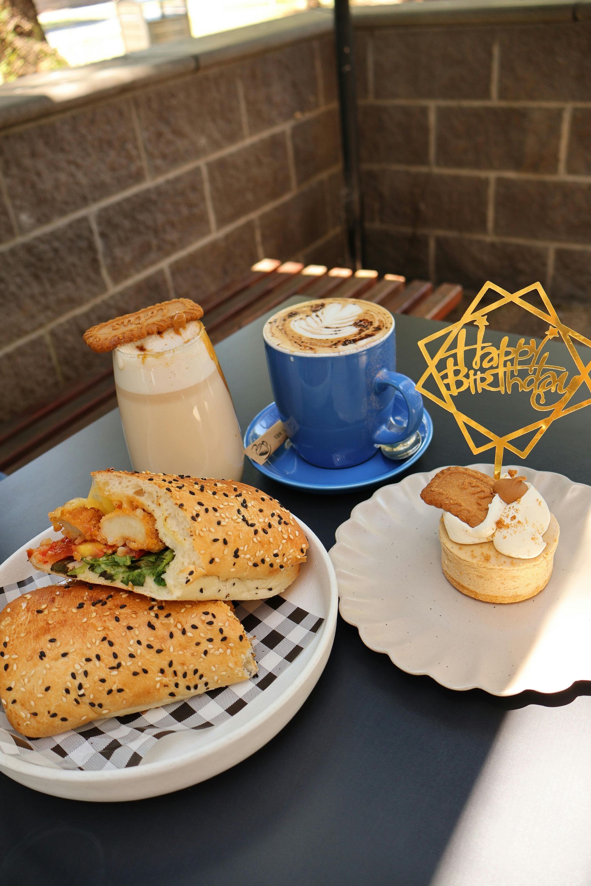 Café, pasteles y sándwiches en platos sobre una mesa de café, con un letrero decorativo dorado.