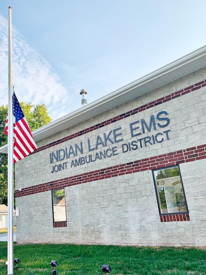 The Indian Lake EMS Joint Ambulance District building featuring a U.S. flag flying at half-staff on a sunny day.