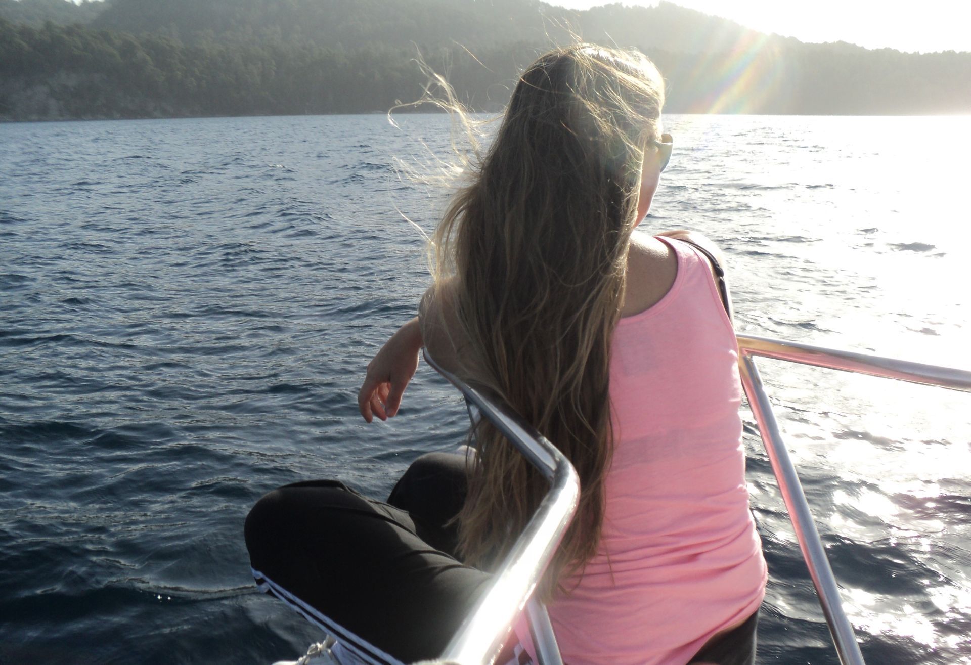Una persona de pelo largo sentada en el borde de un barco, contemplando el mar iluminado por el sol.
