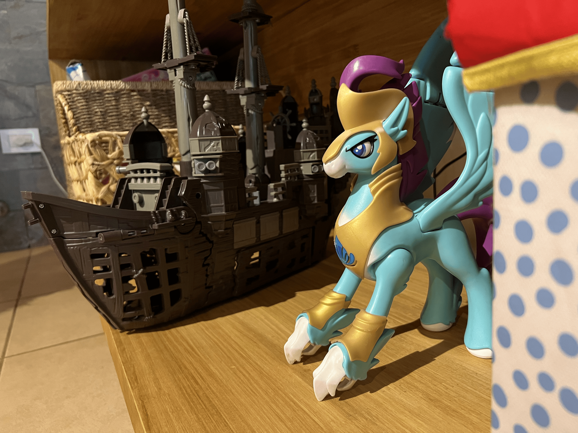 Un juguete My Little Pony de color azul claro con armadura dorada está sobre un estante junto a un gran barco pirata de juguete de color oscuro.
