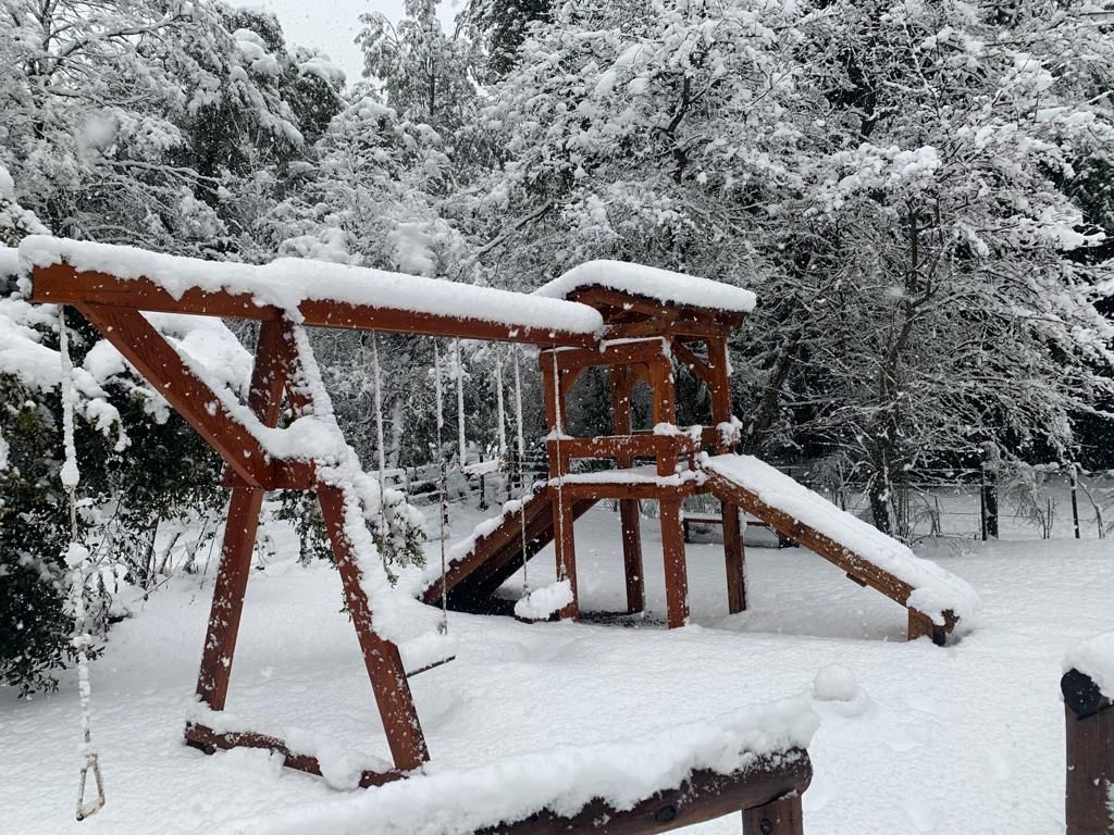 Una estructura de juegos de madera instalada en un patio trasero, cubierta por una gruesa capa de nieve fresca y blanca de invierno.