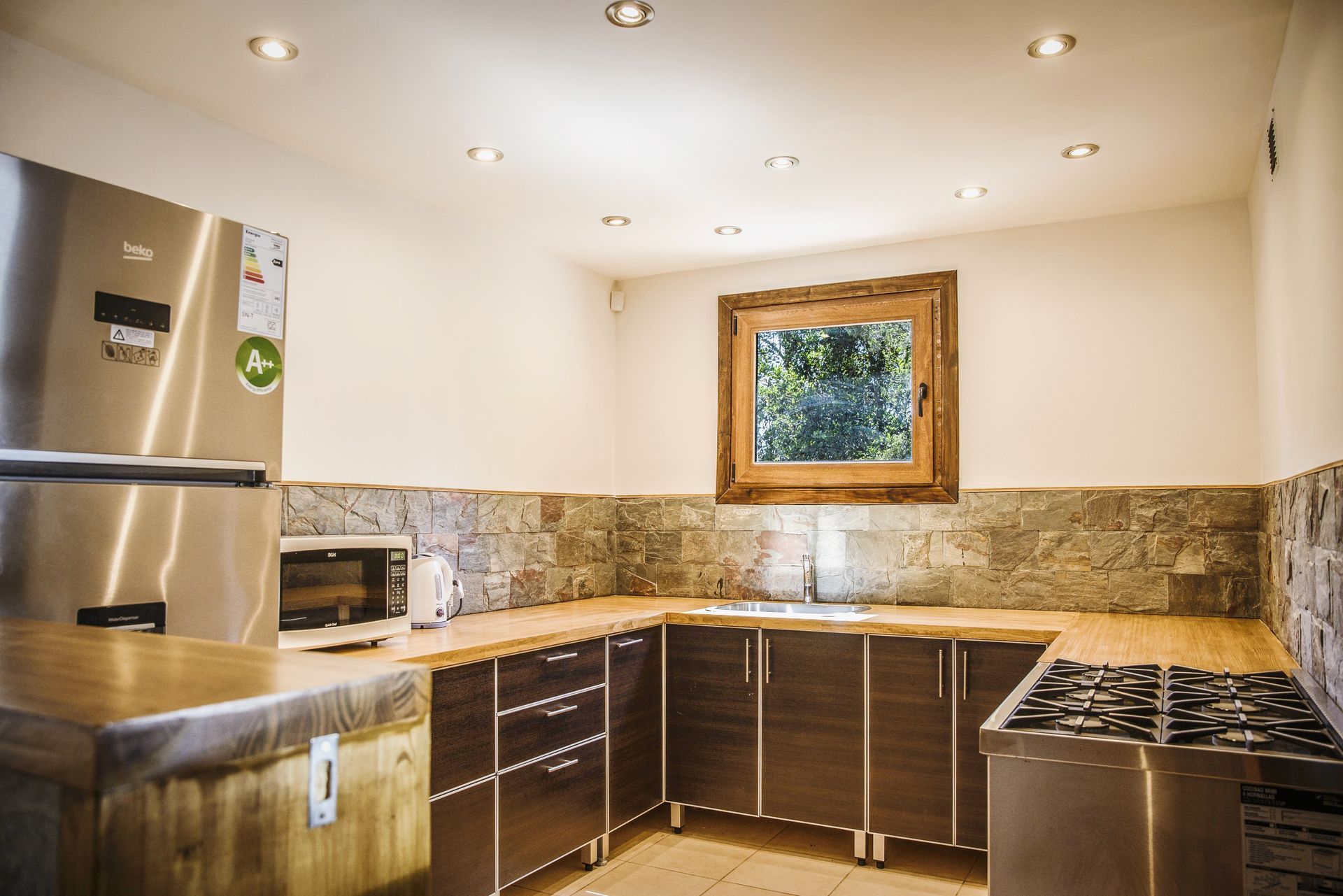 Una cocina moderna con armarios marrones, electrodomésticos de acero inoxidable, un protector contra salpicaduras de piedra y una encimera de madera.
