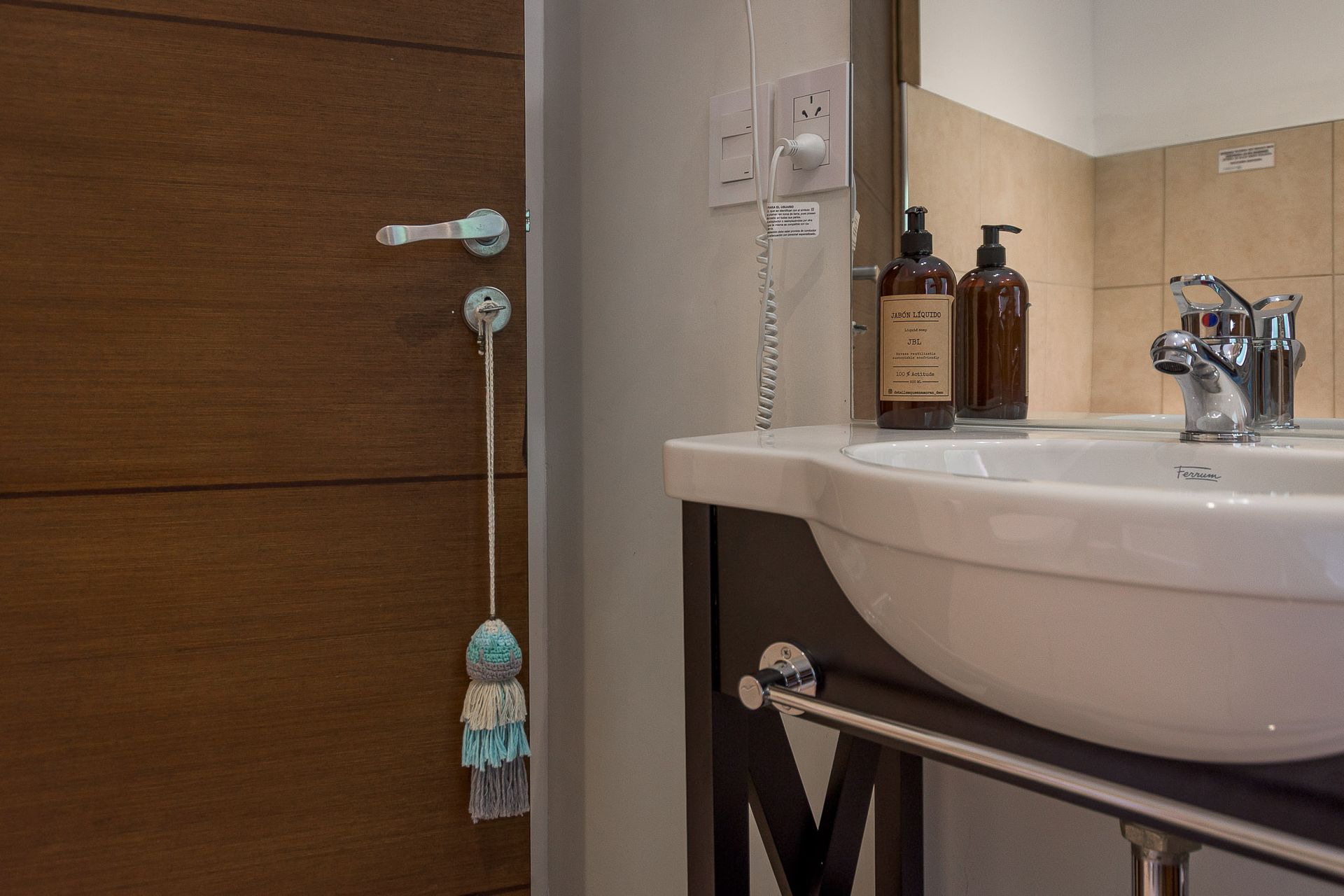 Un lavabo con dos dispensadores de agua se encuentra junto a una puerta de madera decorada con una borla de macramé colgante.